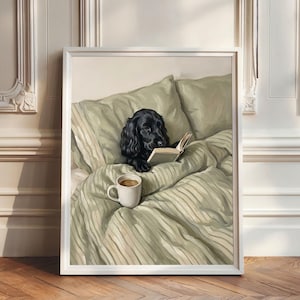 May include: A framed wall art print depicting a black spaniel dog lying in a bed with sage green striped bedding and pillows. The dog is holding an open book with its paws, and a white ceramic mug filled with coffee sits on the bed covers.