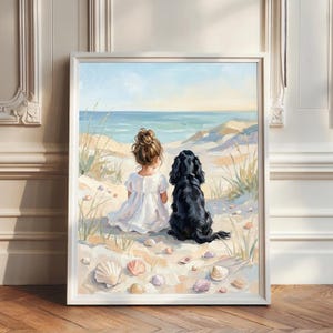 Könnte beinhalten: Ein gerahmter Kunstdruck, der ein Kind mit Dutt in einem weißen Kleid zeigt, das neben einem schwarzen Hund auf einem Sandstrand sitzt. Die Szene umfasst hohes Strandgras, verstreute Muscheln und einen ruhigen blauen Ozean.