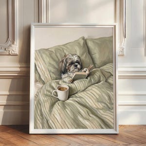 May include: A framed wall art print depicting a small, fluffy, brown and white Shih Tzu dog lying in a bed with sage green striped bedding. The dog is holding an open book with its paws, and a white ceramic mug sits on the bed covers nearby.