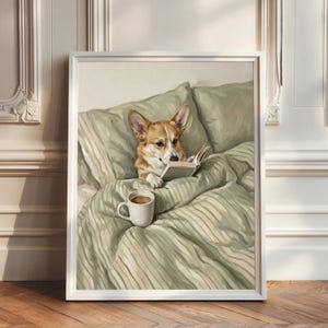 May include: A framed wall art print depicting a tan and white Corgi dog lying in a bed with sage green striped bedding. The dog is holding an open book with its paws, and a white ceramic mug filled with coffee sits on the rumpled bed covers.