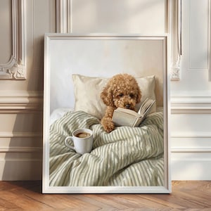 Puede incluir: Impresión enmarcada de un caniche marrón leyendo un libro en la cama, con una taza de café. El perro está bajo una manta y almohada a rayas. La obra de arte está en un marco blanco, contra una pared neutra.
