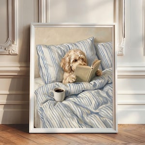 Può includere: Una stampa artistica incorniciata che raffigura un cane dal pelo chiaro e riccio seduto a letto con lenzuola a righe blu e bianche. Il cane tiene un libro aperto tra le zampe e accanto si trova una tazza di ceramica bianca con caffè nero.