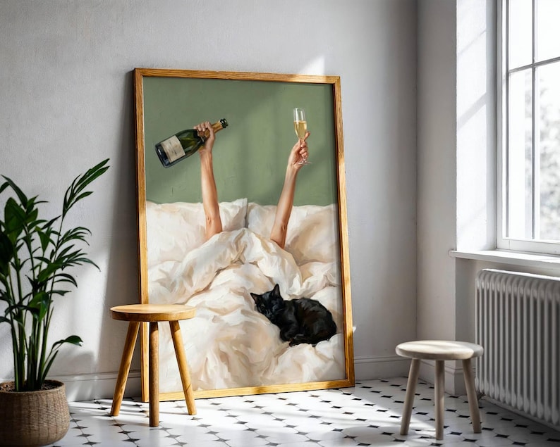 May include: A framed wall art print featuring a green background with two arms reaching up from white bedding, one holding a champagne bottle and the other a champagne flute. A black cat is curled up on the white bed sheets in the foreground.