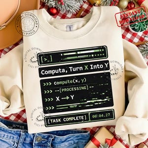 May include: A cream-coloured sweatshirt featuring a black and green graphic with the text "Computa, Turn X Into Y" in a computer code style. The design includes "compute(x, y)" and "TASK COMPLETE".