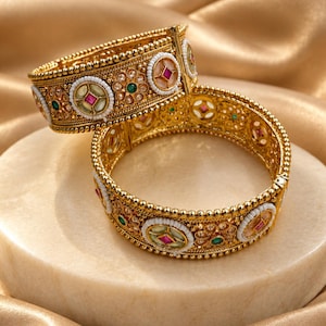 Peut inclure: Deux bracelets rigides en métal doré avec des bords perlés complexes et des motifs circulaires. Chaque bracelet est orné de petites perles blanches, de pierres vertes incrustées et d'accents centraux en forme de losange rose.