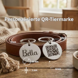 Könnte beinhalten: Zwei runde, silberne Haustieranhänger mit Schlüsselringen. Ein Anhänger hat den Namen "Bella" in Schreibschrift, der andere einen QR-Code. Ein braunes Lederhalsband und ein Hundespielzeug sind im Hintergrund. Die Anhänger haben einen Durchmesser von 2,5 cm und sind 2 mm dick.