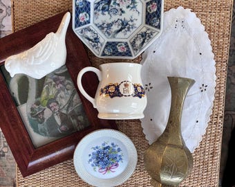 May include: A collection of items including a white ceramic bird, a wooden picture frame with a vintage print, an octagonal blue and white floral plate, a white mug with a crown logo, a small floral plate, a brass vase, and a white lace doily.