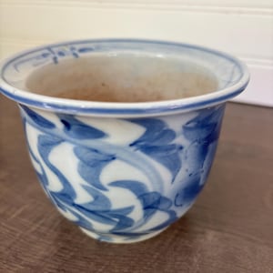 以下が含まれることがあります： 白いベースに手描きの青い花柄が施された小さな陶器のボウル。ボウルには、縁に沿って細い青い線が入った幅広で広がった縁があり、滑らかで丸みを帯びた形状をしています。ボウルの内側は薄いベージュ色をしています。