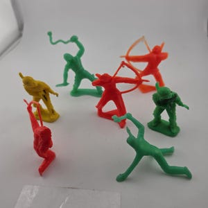 May include: A collection of small, colorful plastic toy soldiers in various poses. The figures are in shades of red, green, yellow, and orange. Some are holding bows and arrows, while others are in action poses.