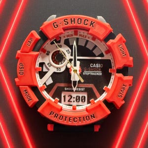 May include: A red and black G-Shock watch displaying 12:00 on its digital screen. The watch face has white, black, and gold detailing, with the text "G-SHOCK" and "CASIO G-SHOCK STEPTRACKER". It features buttons marked "DISP", "LAP", "MODE", "LIGHT", and "START".