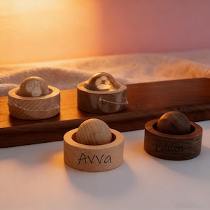 Puede incluir: Cuatro tapones de botella de madera con una parte superior esférica y una base cilíndrica. Un tapón tiene el nombre "Avva" grabado en la base, y otro "Eddien". Los tapones se muestran en una tabla de madera.