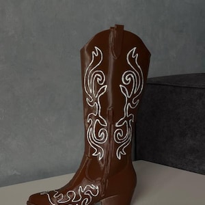 Puede incluir: Una bota vaquera de color marrón con patrones de bordado en blanco a lo largo de la caña y la punta. La bota tiene punta afilada, tacón y una cremallera lateral vertical. El diseño incluye intrincadas líneas blancas en espiral.