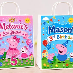 Pode incluir: Duas sacolas de presente de papel branco com alças, com personagens da Peppa Pig. Uma sacola diz "Melanie's 5th Birthday" com um tema rosa e roxo. A outra diz "Mason's 3rd Birthday" com um tema azul.