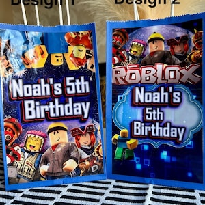 Può includere: Due sacchetti blu per feste con manici bianchi. Ogni sacchetto presenta un design colorato con personaggi di Roblox e la scritta "Noah's 5th Birthday". Il design 1 ha uno sfondo blu e giallo, mentre il design 2 ha uno sfondo blu con il logo Roblox.