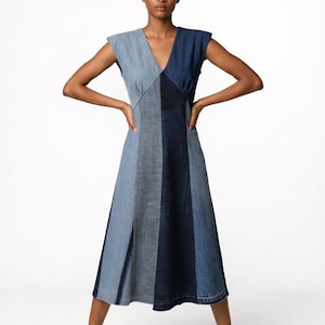 Könnte beinhalten: Ärmelloses Jeanskleid mit V-Ausschnitt und Midirock. Das Kleid hat ein Patchwork-Design mit verschiedenen Blautönen. Das Model steht mit den Händen in den Hüften.