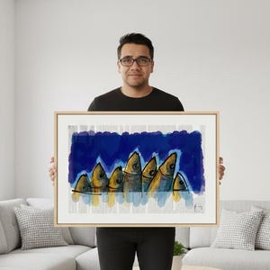 Op de afbeelding: Abstracte kunstprint met een school vissen in goud, blauw en grijs. Het kunstwerk is ingelijst in een licht houten frame. De vissen zijn gestileerd met eenvoudige lijnen en vormen, wat een moderne esthetiek creëert.