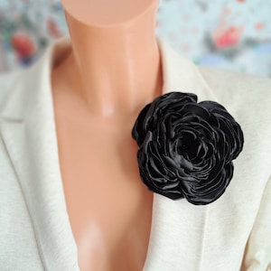 May include: A white blazer with a large black fabric rose pinned to the lapel.