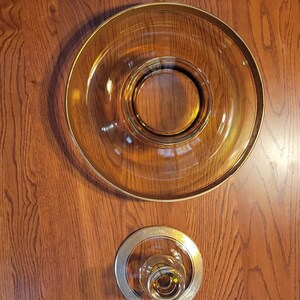 May include: Amber-colored glass serving pieces with gold rims. The set includes a large bowl and two smaller candle holders or coasters, all arranged on a wooden surface.