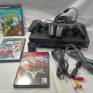 May include: A black PlayStation 2 console with two controllers, three game cases, and a 64MB memory card. The game cases include "Frogger," "Arctic," and "Star Wars: Starfighter." Cables and connectors are also visible.
