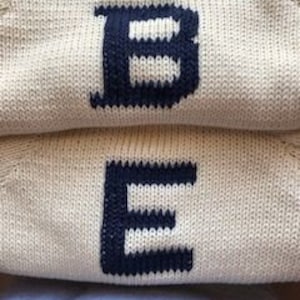 May include: Two cream-colored knitted sweaters with the letters "B" and "E" embroidered in navy blue.