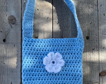 Puede incluir: Bolso de mano de ganchillo azul claro con una correa a juego. El bolso presenta una flor blanca de ganchillo en la parte delantera. El bolso está hecho de un hilo suave y texturizado y es adecuado para objetos pequeños.