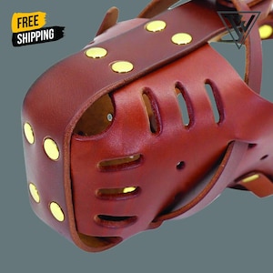 May include: A brown leather dog muzzle with rounded cutouts and gold-coloured rivets. The muzzle has a strap design and is made of a sturdy material. The image also includes the text "FREE SHIPPING" in a yellow and black banner.