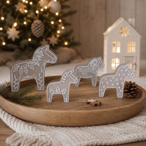 Pode incluir: Quatro figuras de cavalos Dala castanho-claras com padrões de linhas brancas, incluindo motivos florais, de árvores e de estrelas. Os cavalos estão dispostos numa bandeja redonda de madeira, juntamente com uma pequena pinha e dois pequenos ornamentos de madeira.