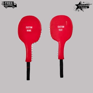 May include: Two red martial arts striking paddles with black handles and white side stitching. The left paddle features the white text CUSTOM NAME, and the right paddle features the white text CUSTOM TEXT. These training tools have a rounded head.