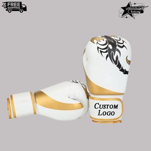 May include: White and gold boxing gloves with a black scorpion design. The gloves have a gold wrist strap with the text "Custom Logo". The gloves are made of leather and are designed for professional use.
