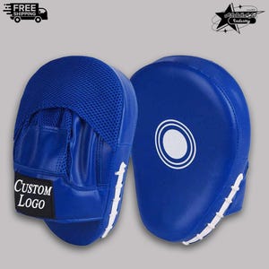 Könnte beinhalten: Zwei blaue Boxhandschuhe mit weißen Akzenten. Einer hat ein Mesh-Oberteil und ein schwarzes Rechteck mit dem Text "CUSTOM LOGO". Der andere hat ein weißes Kreisdesign. Die Handschuhe sind für das Boxtraining konzipiert.