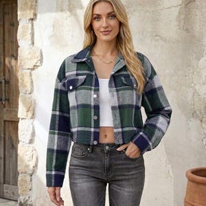 May include: A cropped plaid jacket in shades of green, navy, and gray. The jacket has a collared neckline, button-down front, and two chest pockets. The model is wearing the jacket with a white top and gray jeans.