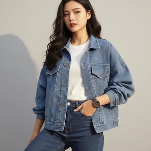 Peut inclure: Veste en jean bleu clair avec col classique, fermeture boutonnée et deux poches poitrine. La veste est associée à un jean bleu foncé et un t-shirt blanc. Une montre est visible au poignet.