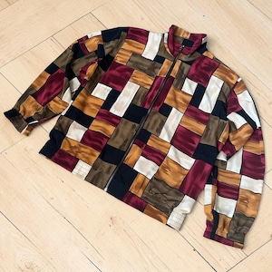 Peut inclure: Veste zippée vintage avec un motif patchwork. La veste présente un col montant, des manches longues et une fermeture éclair sur toute la longueur. La palette de couleurs comprend le bordeaux, le marron, le noir, le beige et le crème. La veste est en matière soyeuse.