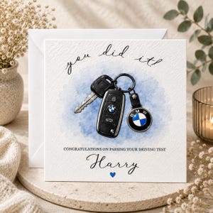 May include: A white card with the words "you did it!" and "Congratulations on passing your driving test". It shows a watercolour illustration of car keys and a BMW keyring. The name "Harry" is written below, with a blue heart.