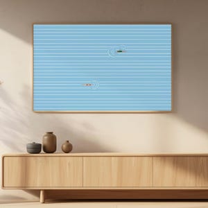May include: A framed art print featuring a minimalist illustration of two swimmers in a pool. The artwork has a light blue background with white horizontal lines, and the swimmers are depicted with simple shapes. The frame is a light brown color.