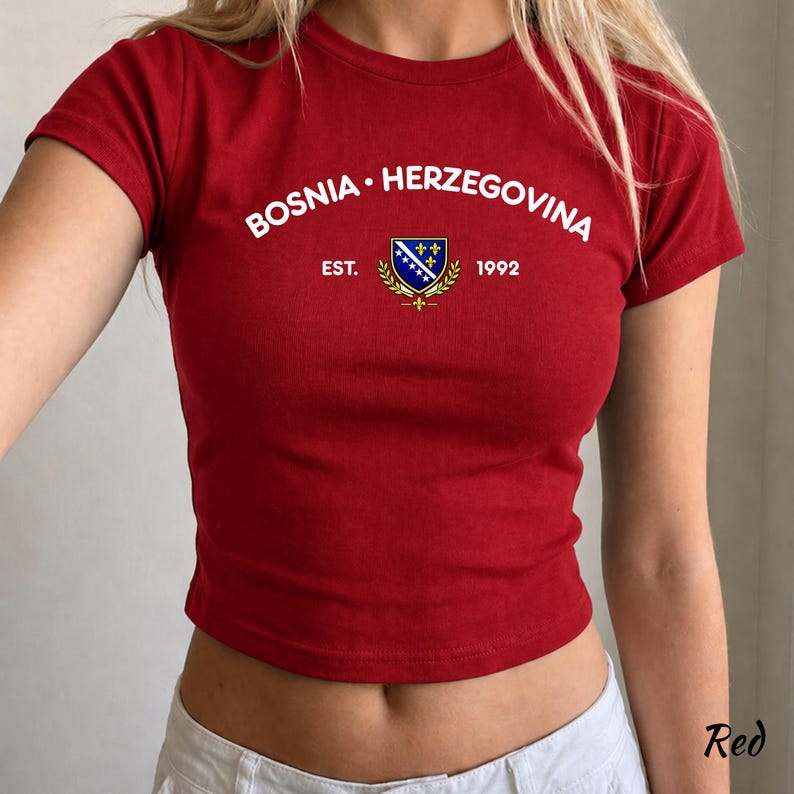 Pu&ograve; includere: Un top corto rosso con la scritta bianca "BOSNIA &bull; HERZEGOVINA", uno stemma e l'anno "1992". La maglietta a maniche corte &egrave; realizzata in un materiale morbido.