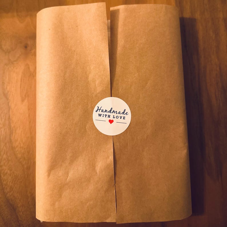 May include: A package wrapped in brown paper, sealed with a white sticker that reads "Handmade WITH LOVE" with a red heart. The package is on a wooden surface.