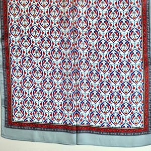 May include: A square scarf with a repeating pattern of blue, red, and turquoise floral motifs on a white background. The border features a red and black design, and the scarf has a light blue border.