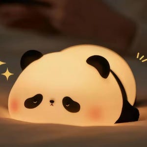 May include: A panda-shaped night light, emitting a soft, warm glow. The panda has black ears, eyes, and paws, and a gentle expression. The light is ideal for a child's bedroom, creating a calming atmosphere.