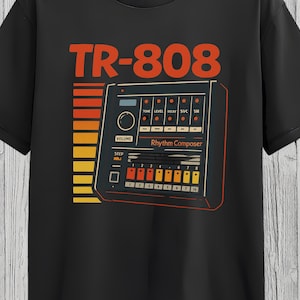 May include: Black t-shirt featuring a retro graphic of a TR-808 Rhythm Composer. The design includes the text "TR-808" in orange, a stylized drum machine, and a gradient of orange and yellow stripes. The words "Rhythm Composer" are also visible.