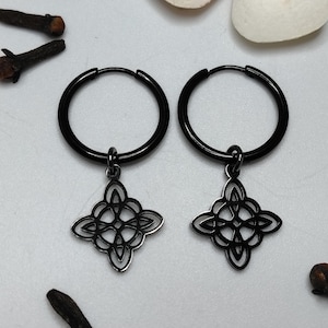 May include: Black hoop earrings with a Celtic knot pendant. The earrings are set against a white background, with cloves scattered around. The earrings have a dark, matte finish and a detailed, openwork design.