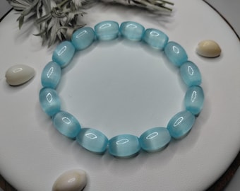 May include: A circular bracelet composed of smooth, translucent light blue oval beads. Each bead features a distinct cat's eye effect, creating a shimmering band of light across the center of the stone. The beads are strung together in a continuous loop.