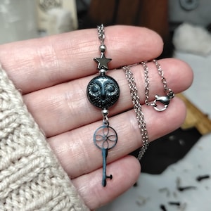 May include: A silver necklace with a star, a circular pendant with a detailed design, and a key-shaped charm. The necklace is shown against a neutral backdrop, emphasising the intricate details of the jewellery.