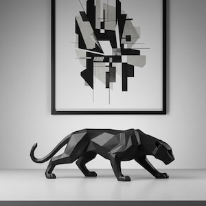 May include: A black geometric panther sculpture with a sleek, modern design. The panther is positioned in a walking pose on a white surface, with an abstract black and white framed artwork in the background.