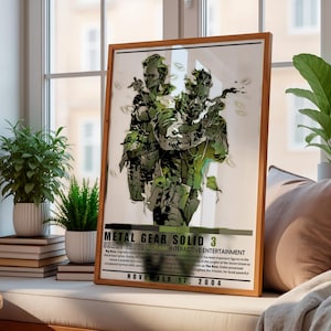 Könnte beinhalten: Ein gerahmtes Poster mit einer stilisierten grün-weißen Illustration zweier Charaktere aus Metal Gear Solid 3: Snake Eater. Der Text enthält den Titel, Konami Interactive Entertainment und das Veröffentlichungsdatum 17. November 2004.