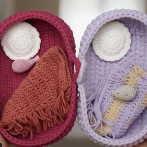 Puede incluir: Dos cestas de ganchillo hechas a mano, una magenta y otra lavanda, cada una llena de artículos de ganchillo. La cesta magenta contiene un círculo blanco, una gota rosa y un paño color óxido. La cesta lavanda contiene un círculo blanco, un ratón gris y un paño lavanda y beige.