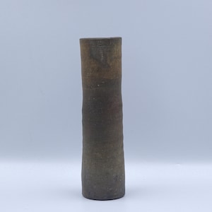 May include: A tall, cylindrical ceramic vase with a rustic, earthy aesthetic. The vase has a dark brown base that gradually transitions to a lighter brown at the top. The surface appears textured, suggesting a handmade quality.