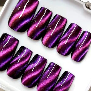 May include: A set of nine press-on nails featuring a deep purple and magenta cat-eye magnetic polish finish. Each nail has a glossy, reflective surface with a diagonal shimmering wave pattern that creates a multidimensional effect across the set.