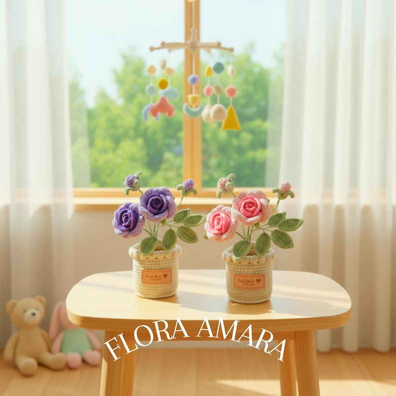 May include: Two crochet flower arrangements in beige pots with the text FLORA AMARA. One pot contains purple roses with green leaves, and the other contains pink roses with green leaves. Each pot features a small rectangular label with text.
