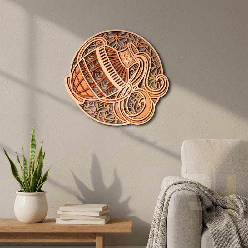 May include: A layered wooden wall art piece depicting the Aquarius zodiac symbol. The artwork features a water bearer design in shades of light brown and orange, set against a circular background with intricate cut-out patterns. The piece is mounted on a neutral-colored wall.